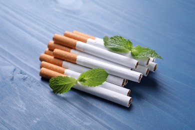 Photo of Menthol cigarettes and mint leaves on blue wooden table