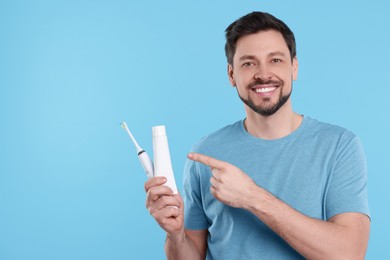 Happy man with electric toothbrush and tube of toothpaste on light blue background. Space for text