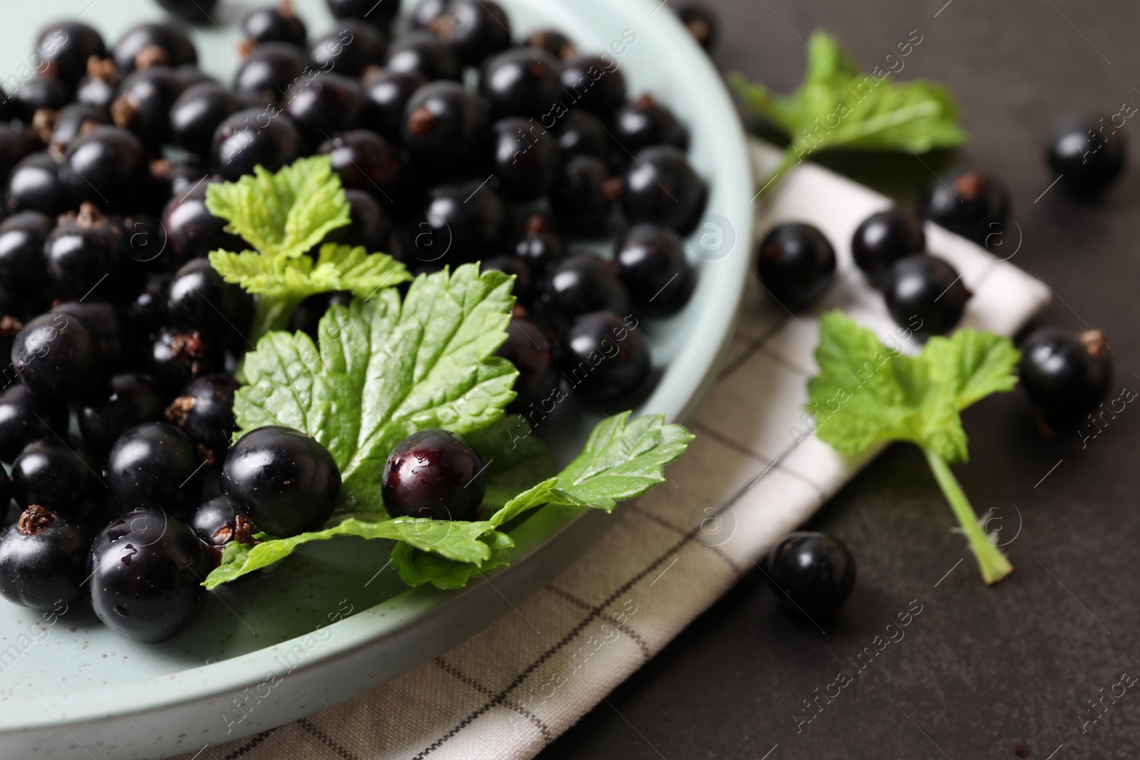 Photo of Plate with ripe blackcurrants and leaves on grey background, closeup