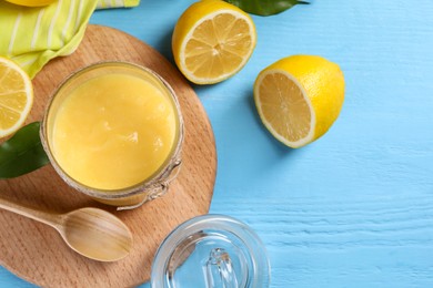 Delicious lemon curd in glass jar, fresh citrus fruit and spoon on light blue wooden table, top view