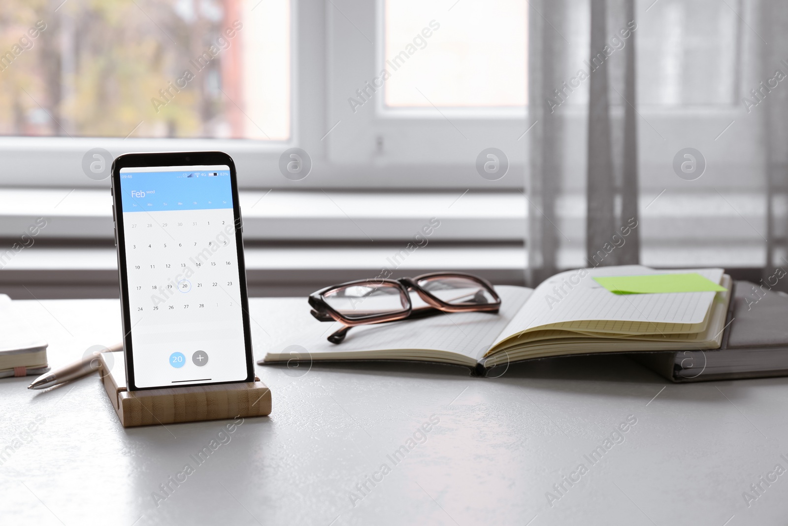 Photo of Modern smartphone with calendar on screen in office