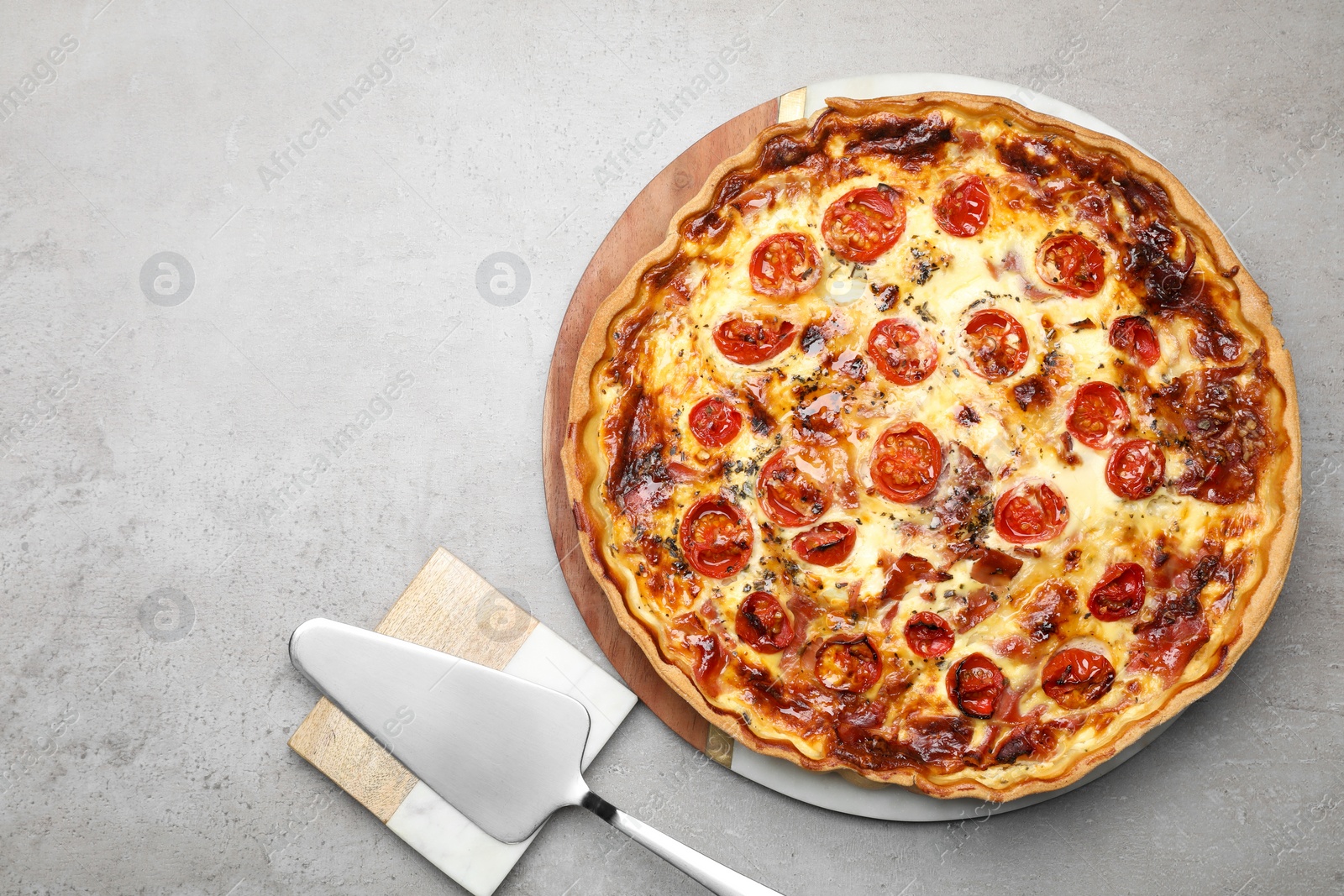 Photo of Delicious homemade prosciutto quiche and spatula on light gray table, flat lay. Space for text