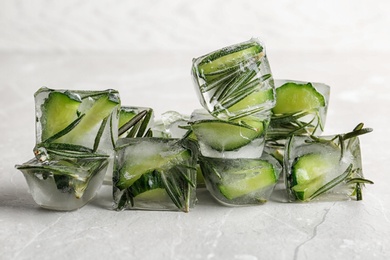 Photo of Ice cubes with cut cucumber and rosemary on light background