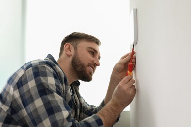 Photo of Man installing security alarm system on light wall at home