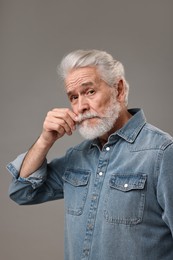 Senior man touching mustache on grey background