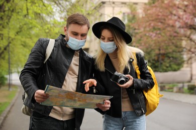 Photo of Couple of tourists in medical masks with map planning trip on city street