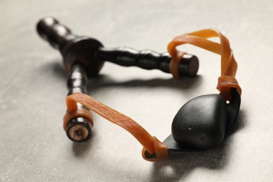 Black slingshot with pebble on light grey table, closeup