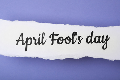 Paper note with phrase APRIL FOOL'S DAY on lilac background, top view
