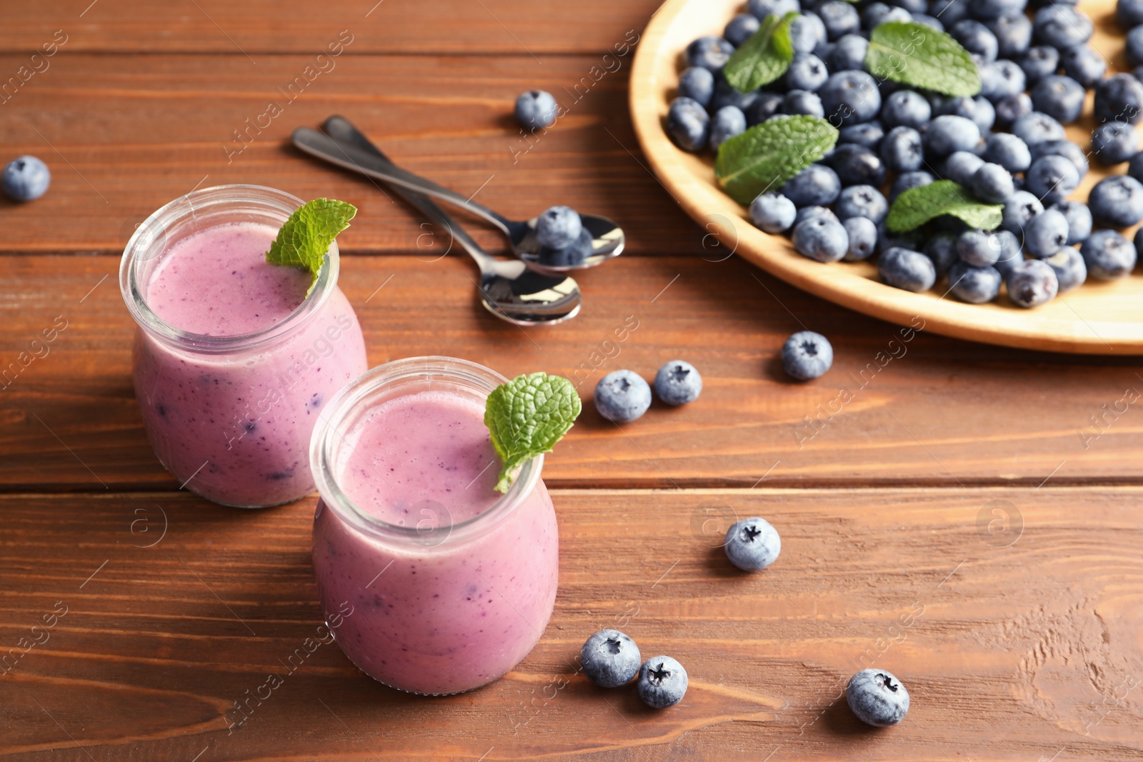 Photo of Tasty blueberry smoothie in jars and berries on wooden table