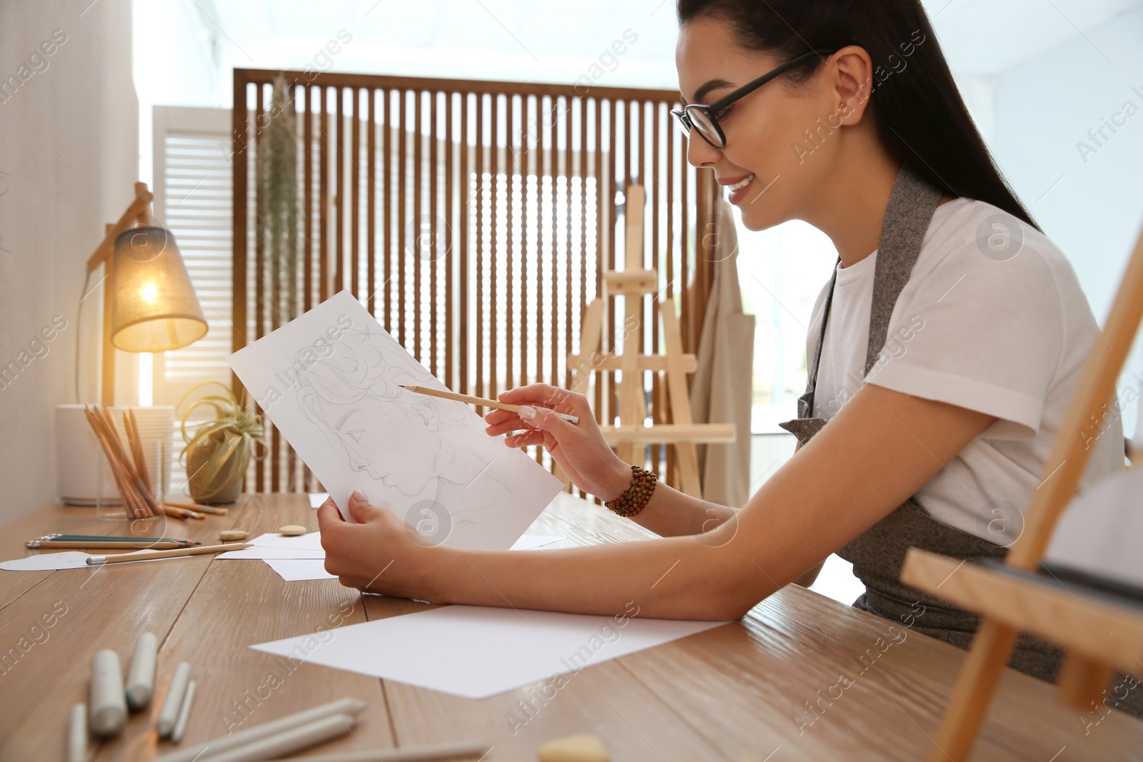 Photo of Young woman drawing male portrait at table indoors