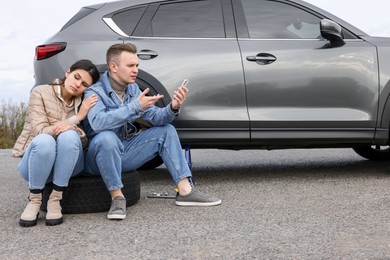 Photo of Young couple with smartphone near car on roadside. Tire puncture