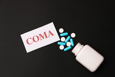 Photo of Card with word Coma and bottle of pills on black background, flat lay