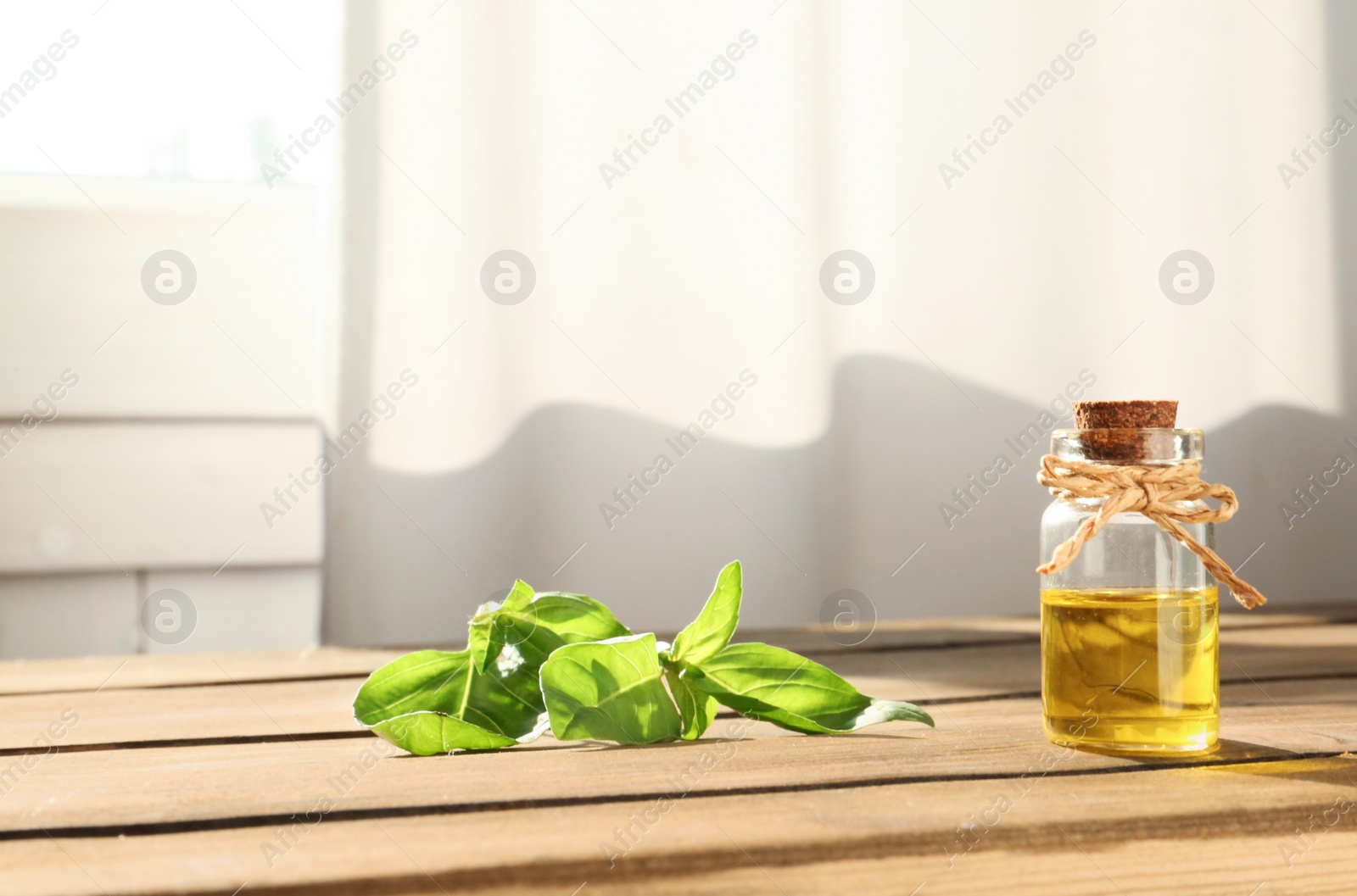 Photo of Bottle of essential basil oil on table against blurred background. Space for text