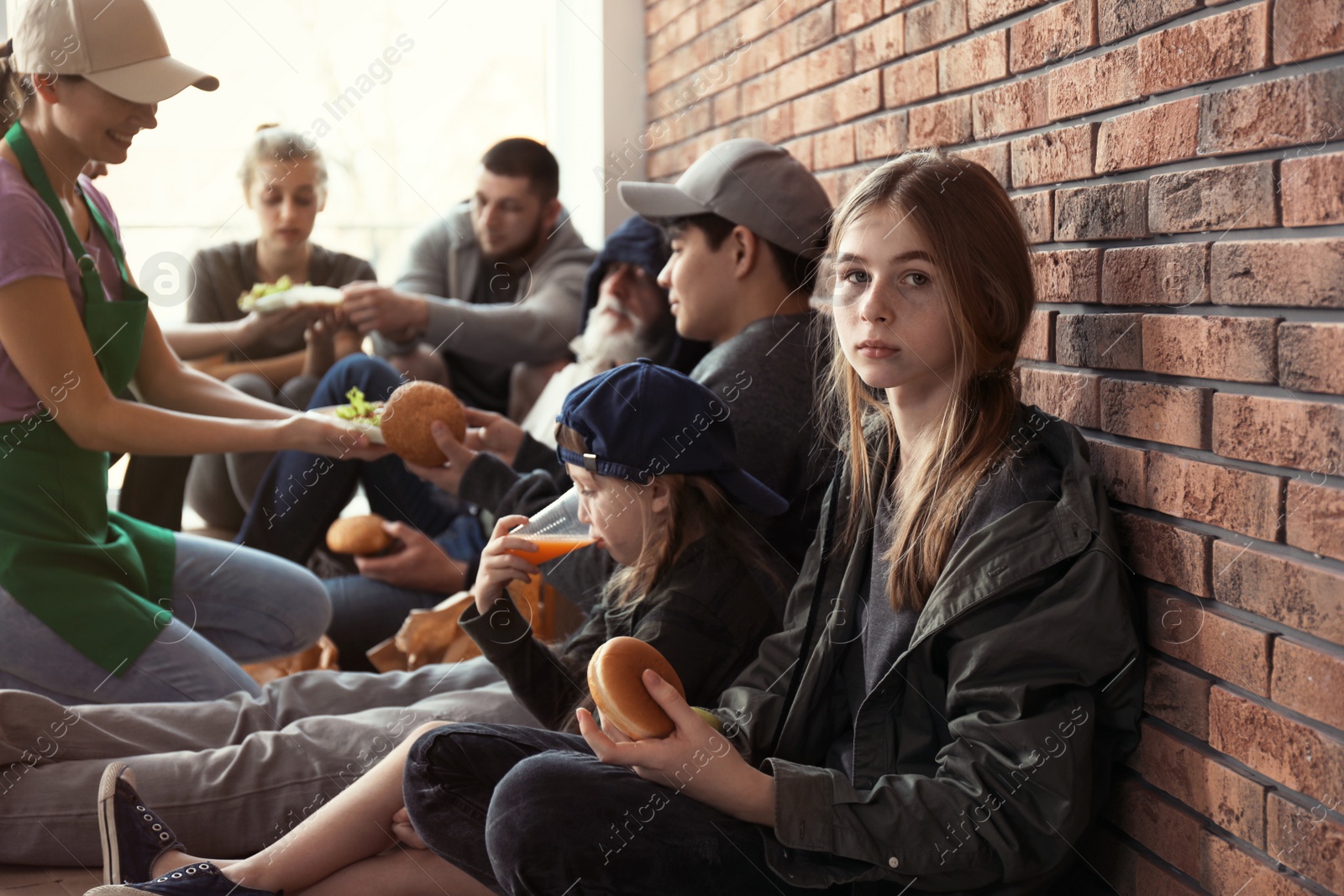 Photo of Teenage girl with other poor people receiving food from volunteers indoors