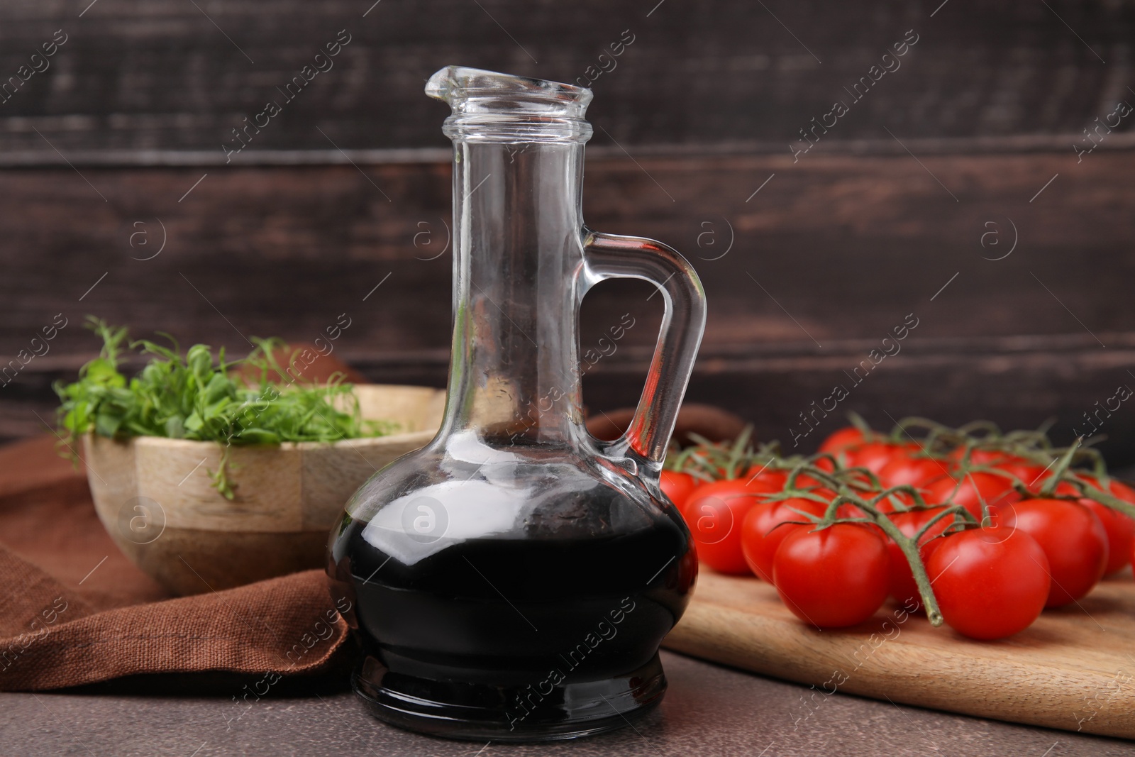 Photo of Organic balsamic vinegar, tomatoes and greens on grey table