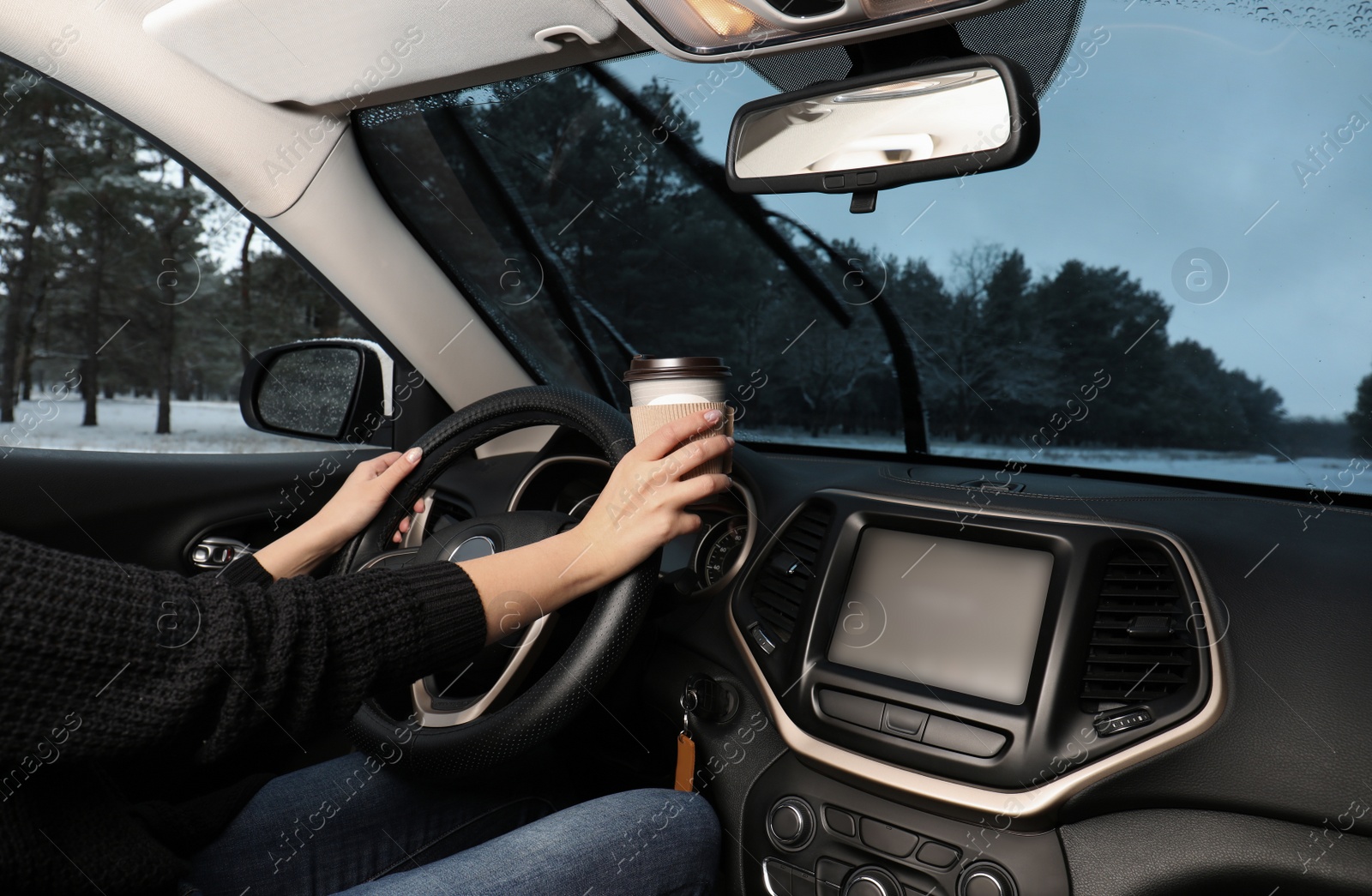 Photo of Young woman with coffee driving car along winter forest, closeup