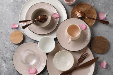 Photo of Stylish table setting. Dishes, cutlery, cup and petals on grey surface, flat lay