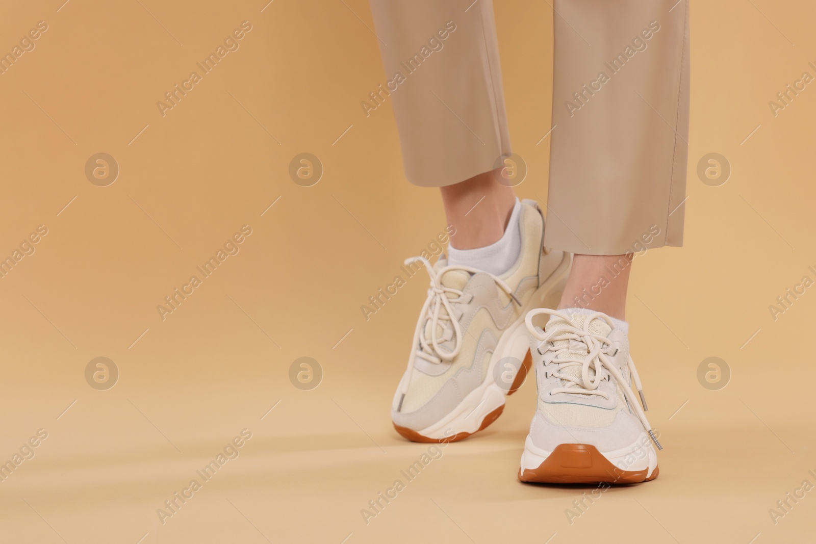 Photo of Woman wearing pair of new stylish sneakers on beige background, closeup. Space for text