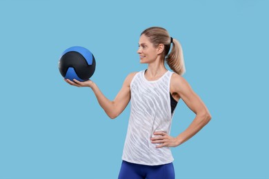 Photo of Portrait of happy sportswoman with medicine ball on light blue background