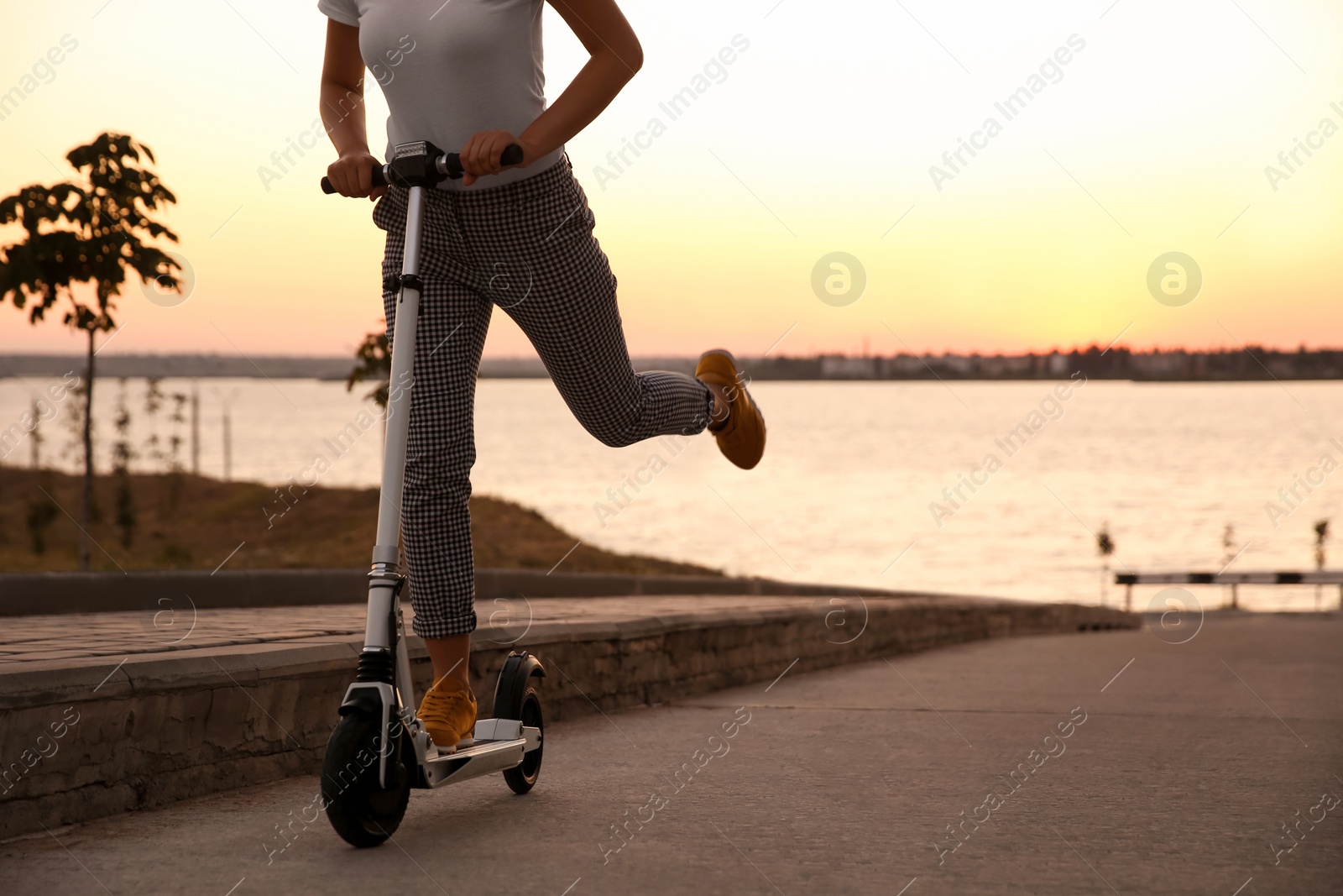 Photo of Woman riding electric kick scooter outdoors at sunset, closeup