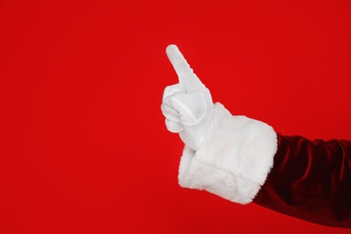 Photo of Santa Claus pointing at something on red background, closeup of hand. Space for text