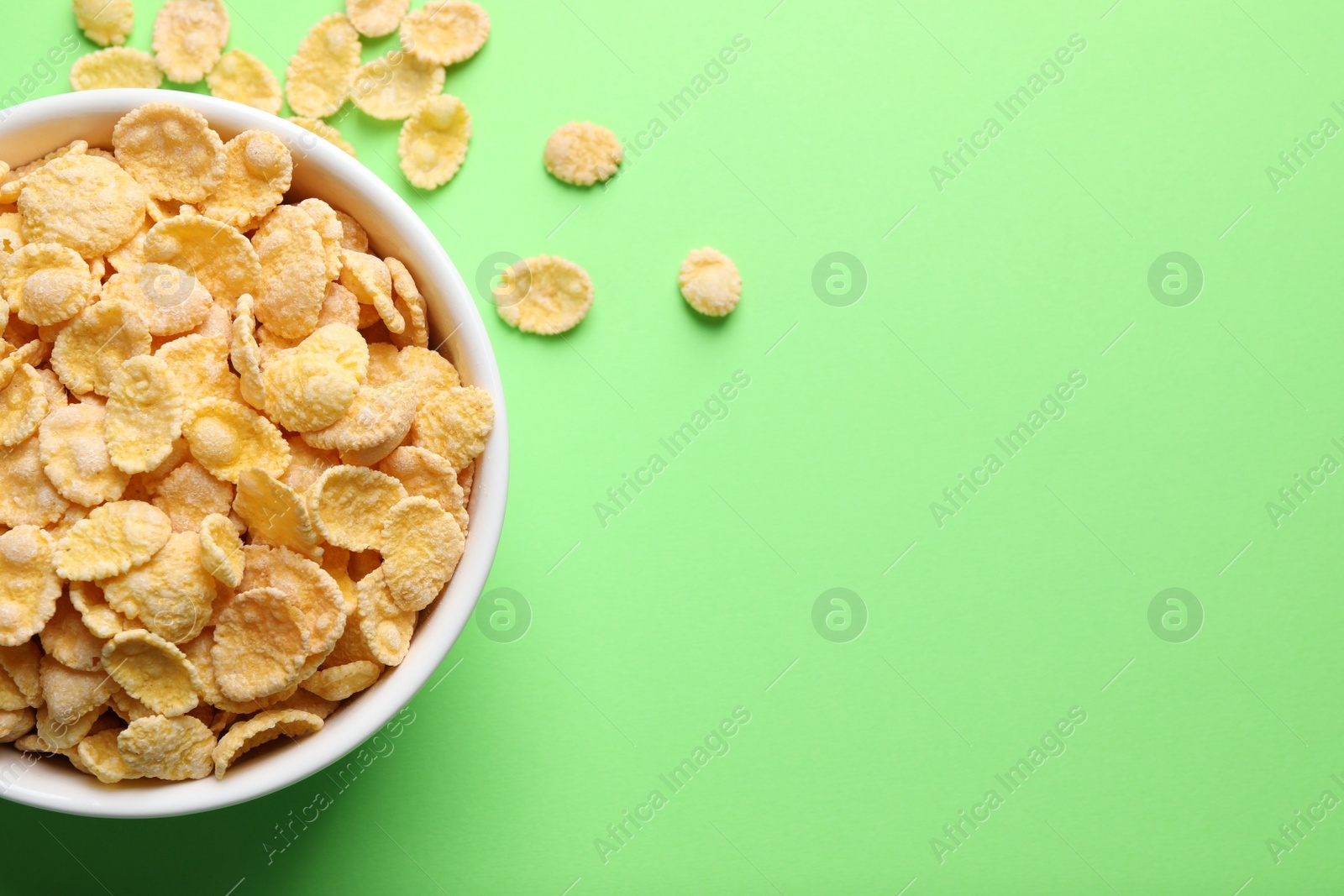 Photo of Bowl of tasty crispy corn flakes on light green background, flat lay. Space for text