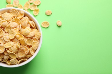 Photo of Bowl of tasty crispy corn flakes on light green background, flat lay. Space for text