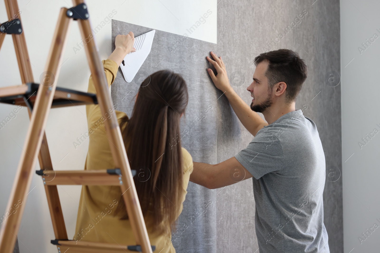 Photo of Couple hanging stylish gray wallpaper in room