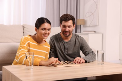 Happy couple playing checkers at coffee table in room