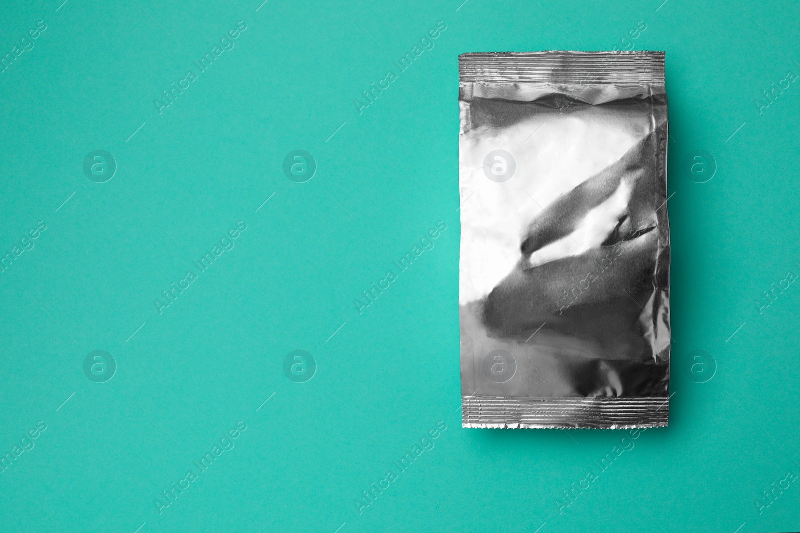 Photo of Blank foil package on turquoise background, top view. Space for text