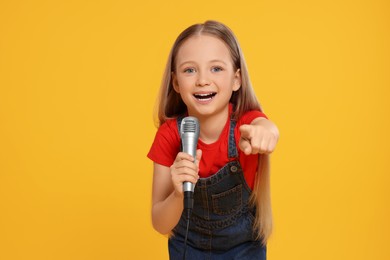 Photo of Cute little girl with microphone singing on yellow background