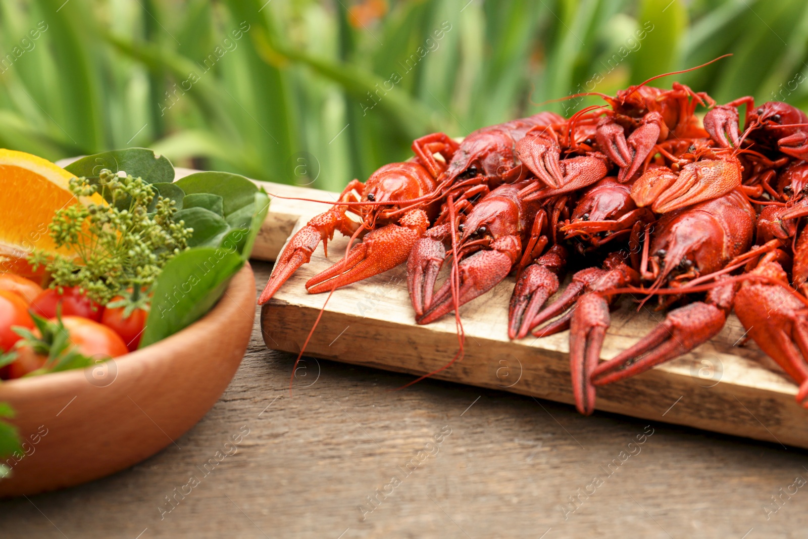 Photo of Delicious red boiled crayfish and products in bowl on wooden table