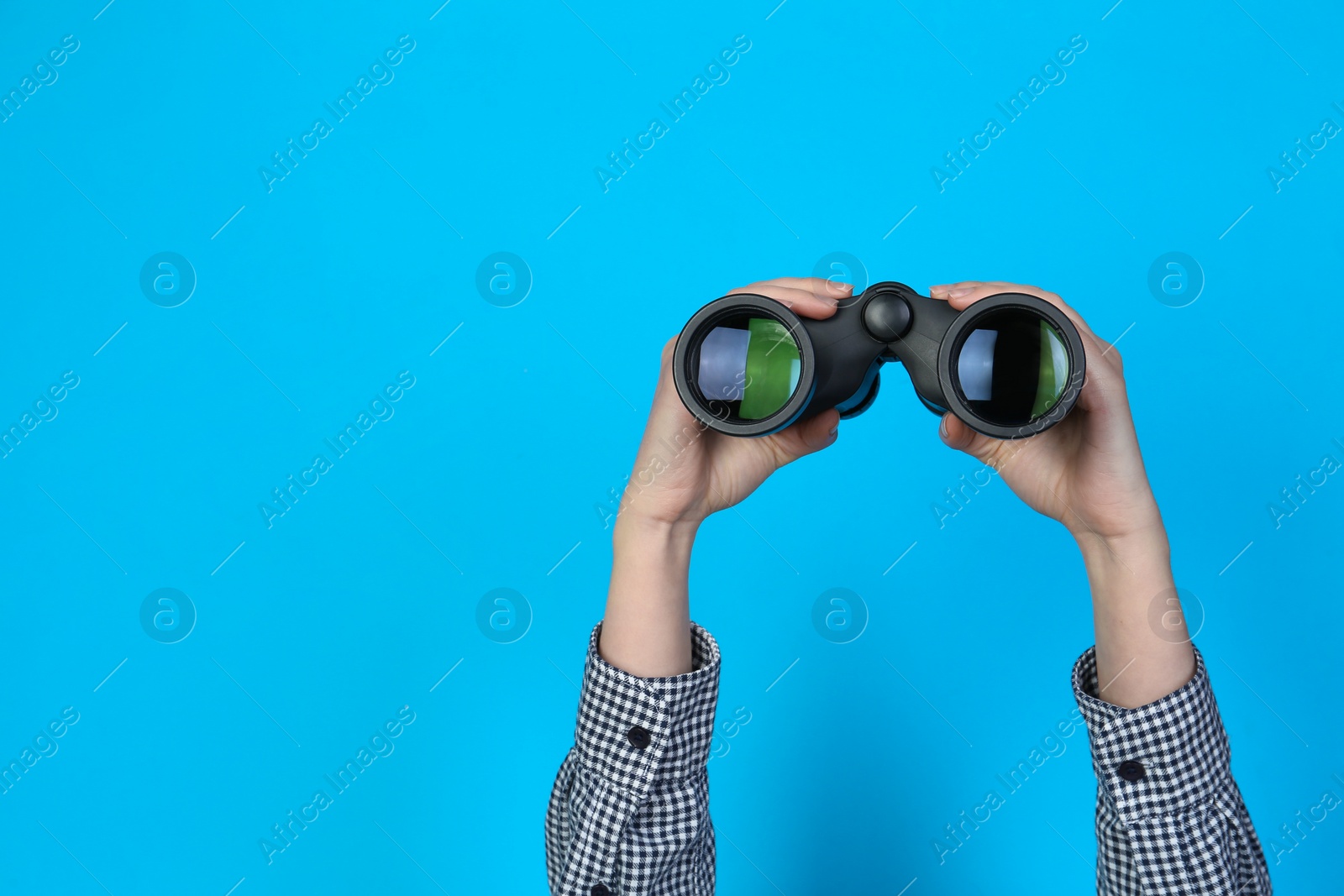 Photo of Woman holding modern binoculars on light blue background, closeup. Space for text