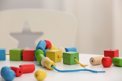 Photo of Wooden pieces and string for threading activity on white table. Motor skills development