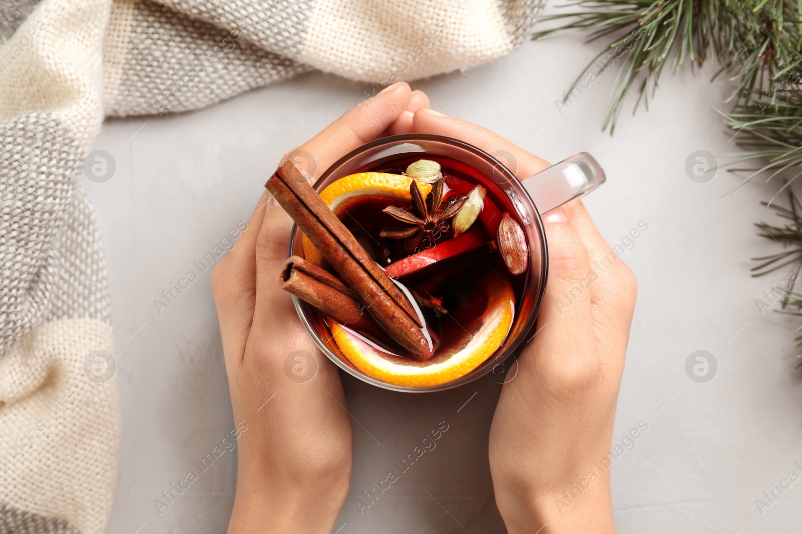 Photo of Woman holding cup of tasty mulled wine at grey table, top view