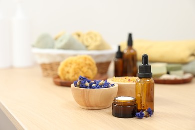 Photo of Bottle of essential oil, dry flowers and jar with cream on light wooden table. Spa therapy