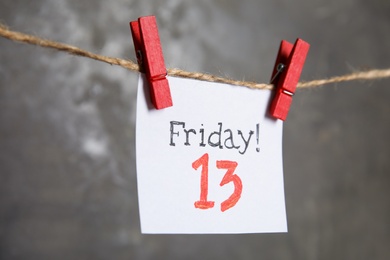 Photo of Paper note with phrase Friday! 13 hanging on twine against grey background. Bad luck superstition