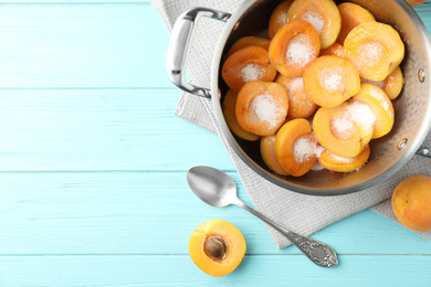 Photo of Pot with apricots and sugar on light blue wooden table, space for text. Making delicious jam