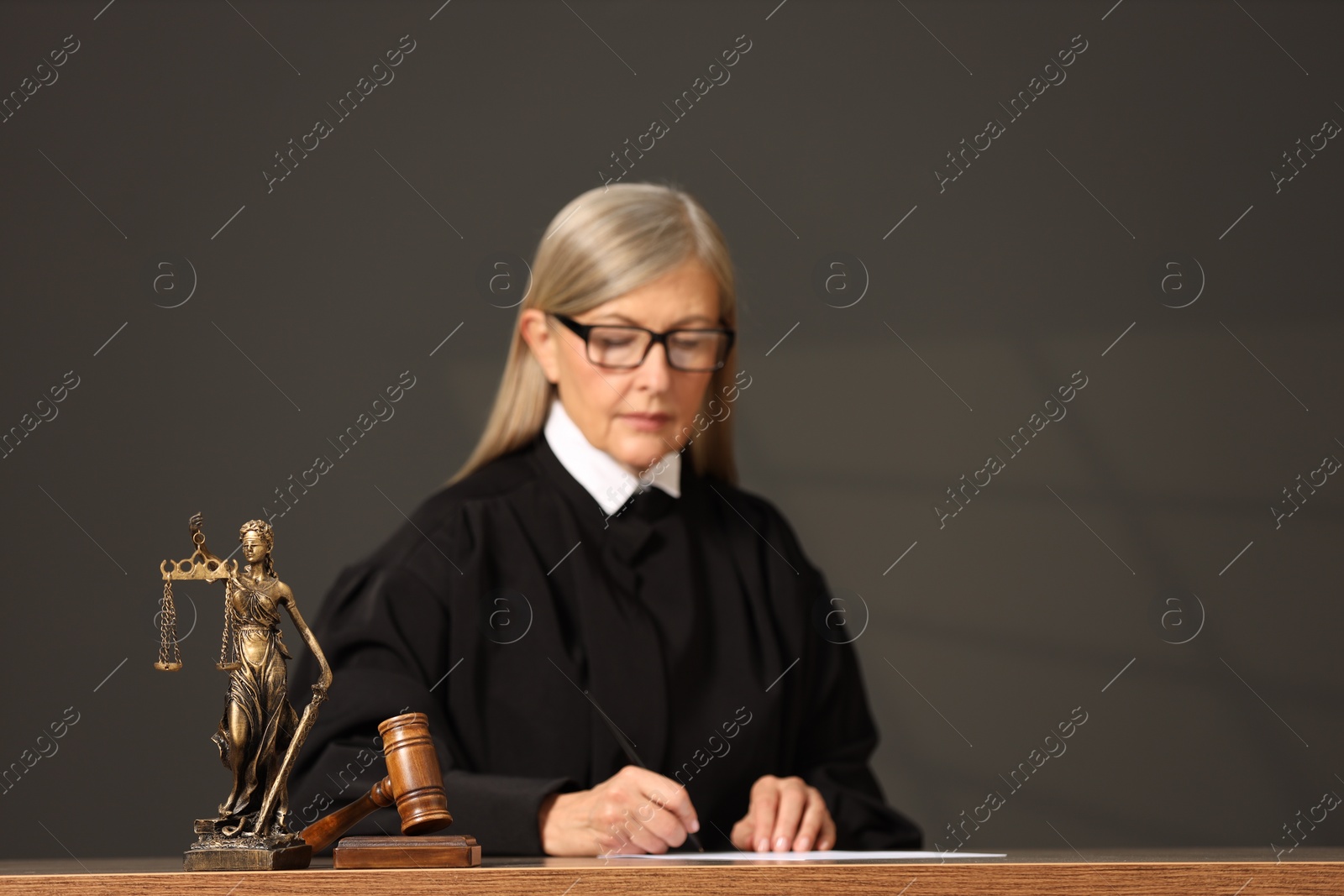 Photo of Judge working with document indoors, selective focus. Mallet and figure of Lady Justice on wooden table