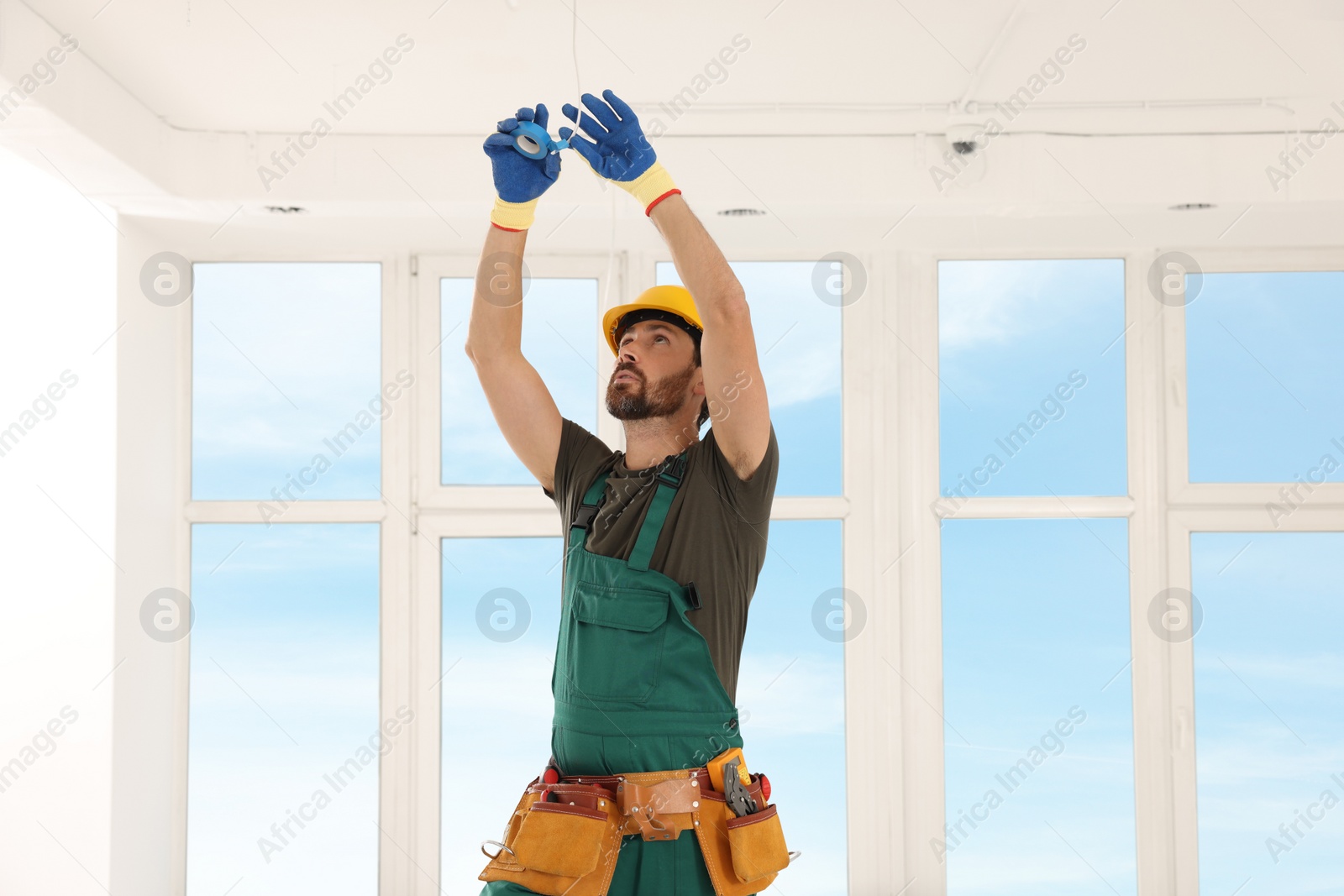 Photo of Electrician fixing wires with insulating tape indoors