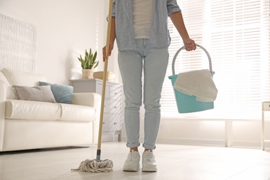 Woman with mop and bucket in room, closeup. Cleaning supplies