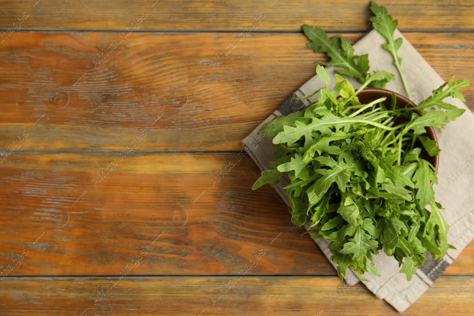 Photo of Fresh arugula in bowl on wooden table, flat lay. Space for text