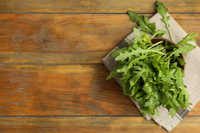 Fresh arugula in bowl on wooden table, flat lay. Space for text