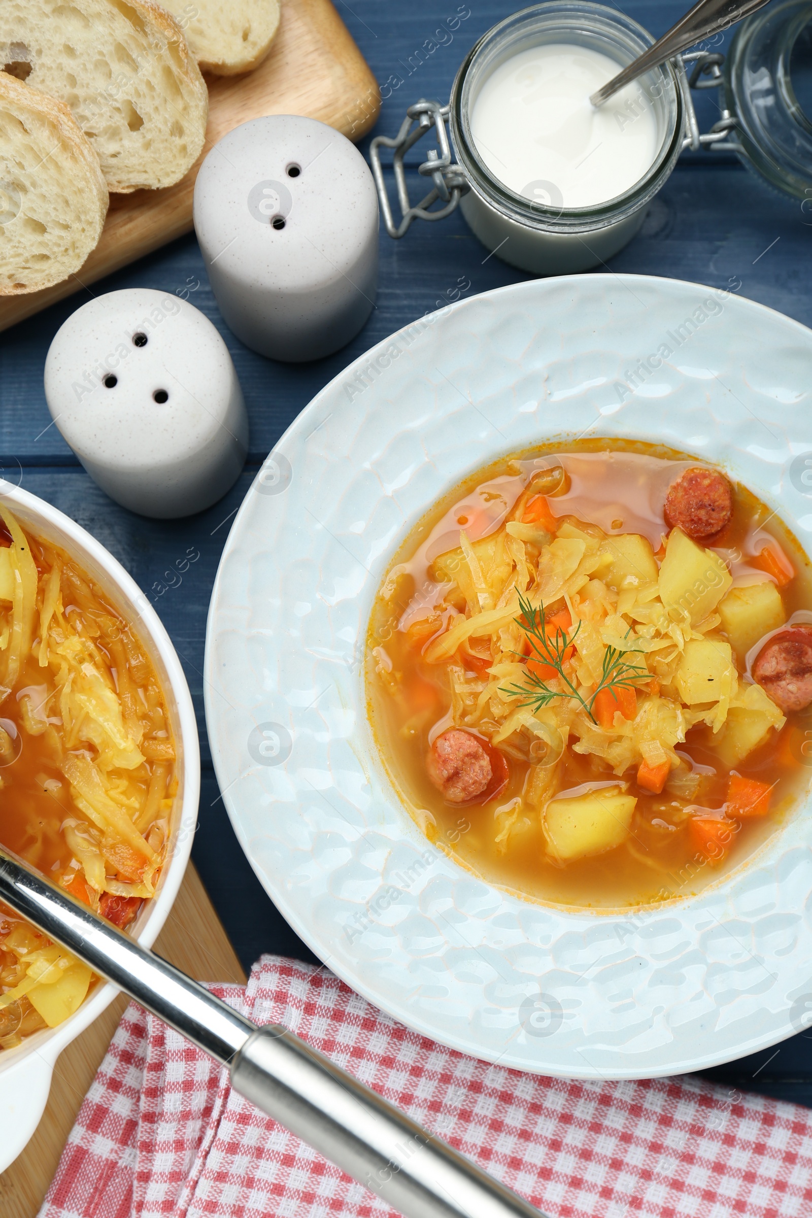 Photo of Delicious sauerkraut soup with smoked sausages served on blue wooden table, flat lay