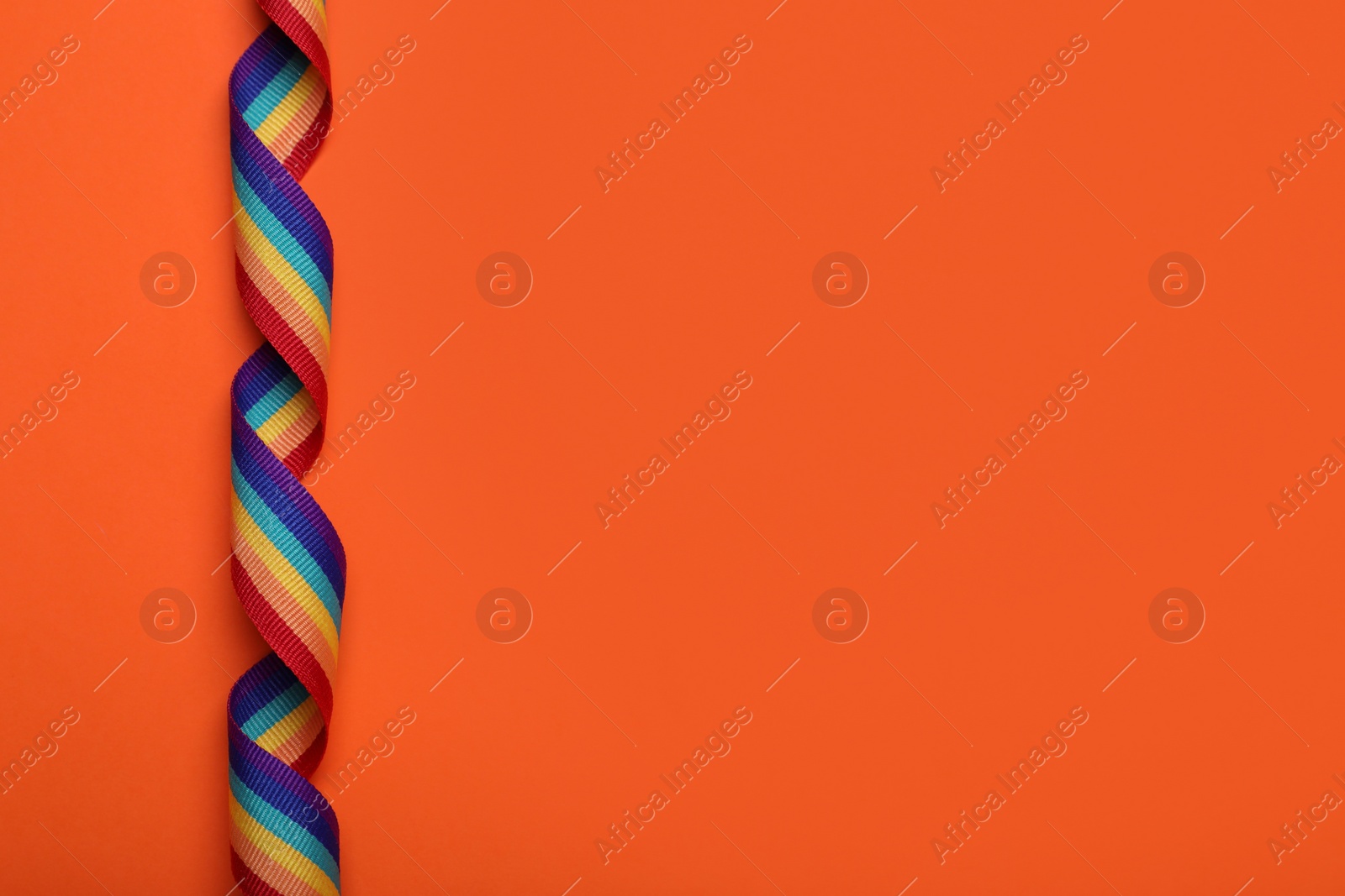 Photo of Rainbow ribbon on orange background, top view with space for text. LGBT pride