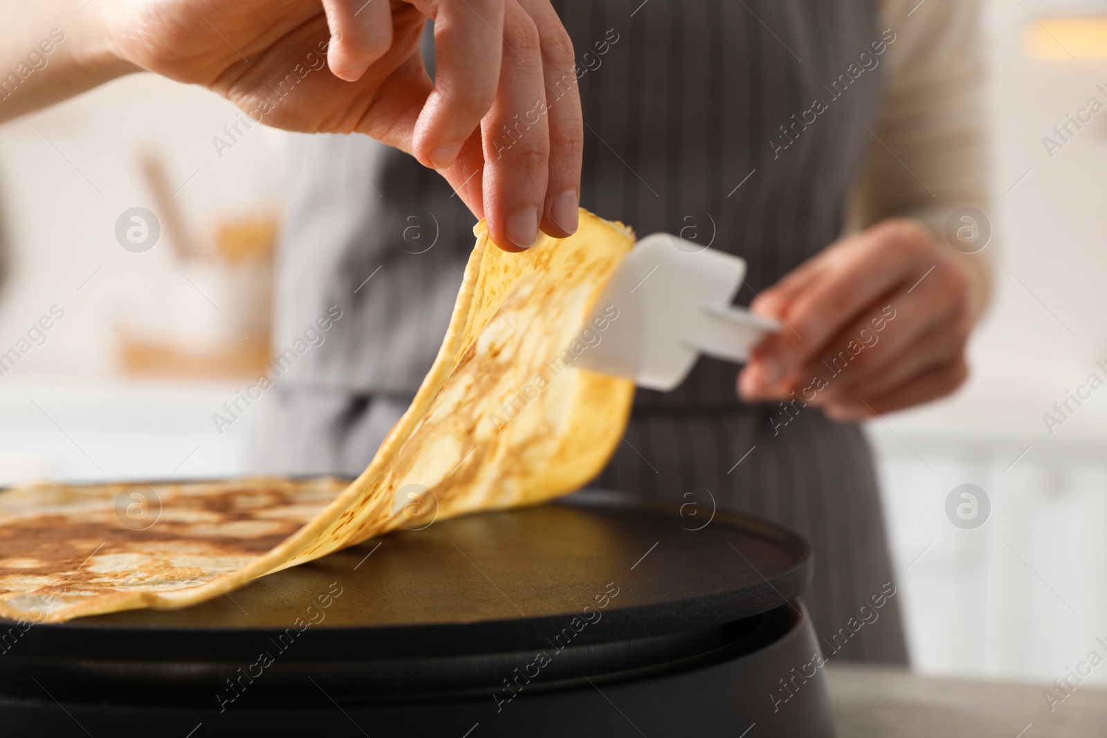 Photo of Woman cooking delicious crepe on electric pancake maker in kitchen, closeup