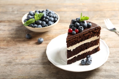 Plate with slice of chocolate sponge berry cake on wooden background