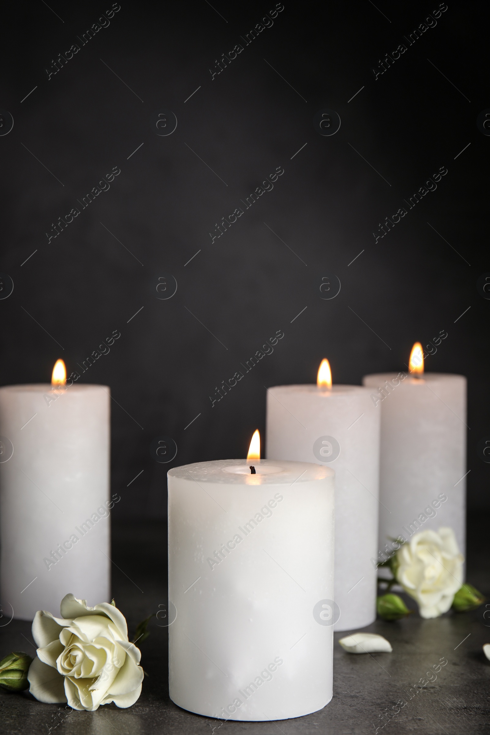 Photo of Burning candles and beautiful flowers on grey table, space for text