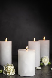 Photo of Burning candles and beautiful flowers on grey table, space for text