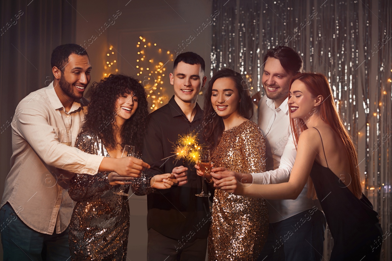 Photo of Happy friends with glasses of wine and sparklers celebrating birthday indoors